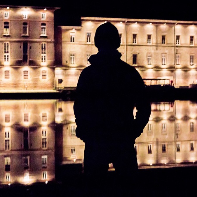 Un Nocturne pensif debout dans la nuit, contemplant les façades éclairées au bord de la Garonne à Toulouse.